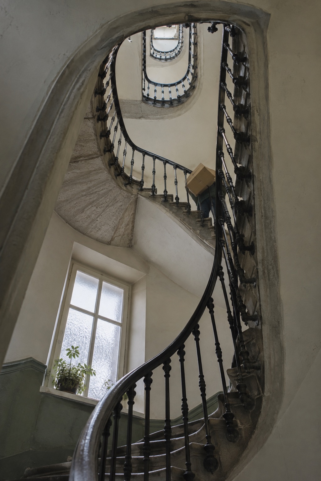 Une cage d’escalier ancienne en colimaçon vue depuis le bas, avec une rampe en fer forgé.